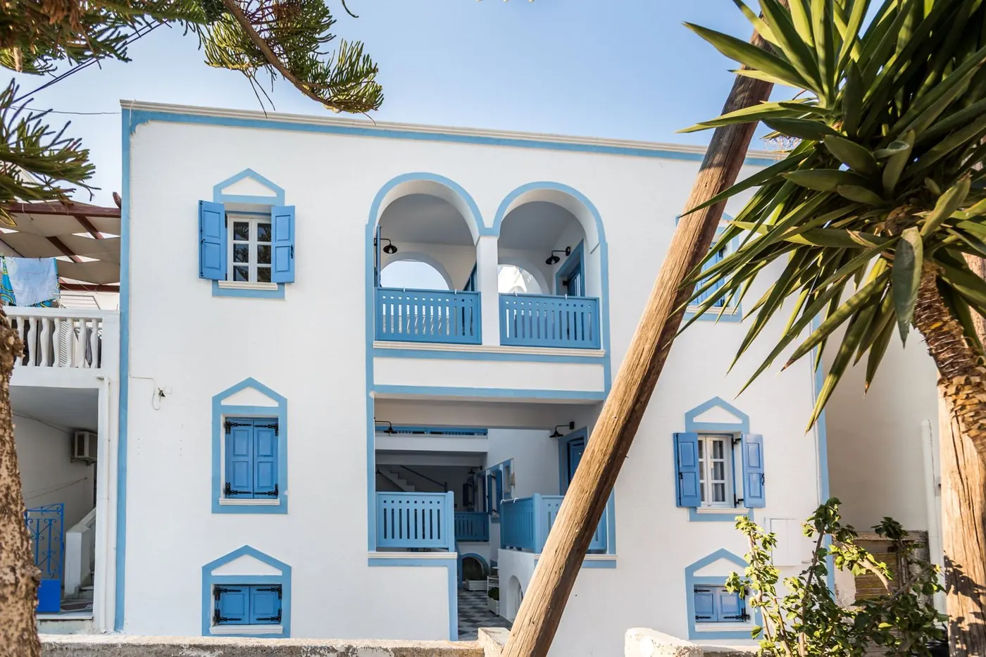 Η λευκή πρόσοψη του Fanouris Condo με μπλε παραθυρόφυλλα και τοξωτά μπαλκόνια